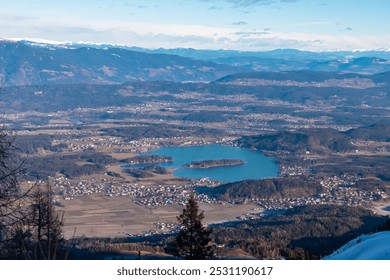 Panoramic aerial view of picturesque alpine lake Faak seen from Karawanks, Carinthia, Austria Slovenia border. Vibrant blue waters contrasting with surrounding green forests and snow-capped mountains - Powered by Shutterstock