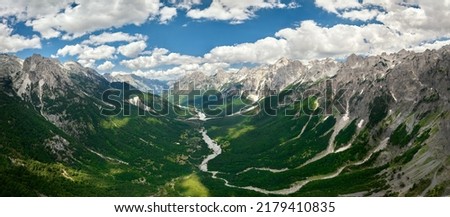 Panoramic, aerial view of the scenic Valbona river valley, green valleys, blue sky with clouds, steep rocks, remnants of snow. Hikers paradise. Theth national park, Albanian Alps, Albania. 