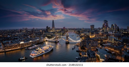 Panorámica, vista aérea del horizonte de Londres con un barco de crucero borroso en movimiento que pasa por debajo del puente de la Torre levantado durante el atardecer, Inglaterra