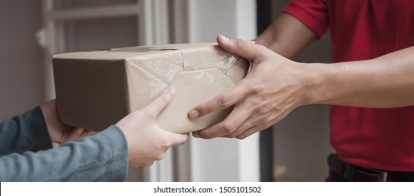 Panoramic Banner. Delivery Service Man In Red Uniform With Woman Customer Receiving Parcel Post Box From Courier At Home, Cargo Shipping, Express Delivery Service, Online Shopping And Logistic Concept