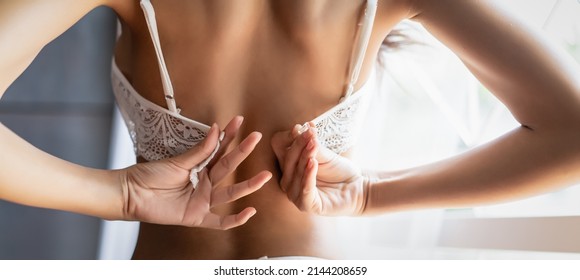 Panoramic banner image of back view of beautiful sexy woman unhooking and taking off or putting on her white lace underwear bra rear view in boudoir room. Wide crop, web page,template with copy space.