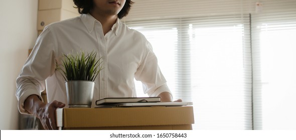 Panoramic Banner. Losing Job. Stressed Asian Young Employee Business Man Leaving The Office With His Personal Stuff Carton Box, Financial Crisis, Unemployed, Fired From Job And Lay Off Concept