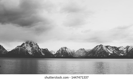 A panoramic beautiful grayscale photography of sea surrounded by mountains and grey clouds - Powered by Shutterstock