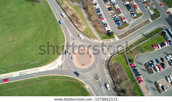 Panoramic bird\'s-eye aerial view of\
traffic navigating a small road roundabout in the\
UK.