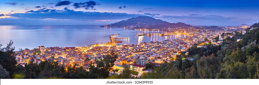 Panoramic city and port view on the island of Zakynthos, Greece. Incredibly romantic sunrise on Zakinthos. Amazing sunset view on Zante town with multicolored clouds. Street lights. Port with ferries.