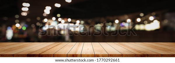 Panoramic clean wood counter table top on blur\
street night cafe background pub coffee desk shop montage dark\
scene, Blurry wide wooden texture shelf bar in luxury restaurant\
food kitchen backdrop
