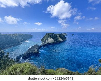 Panoramic clifftop view over deep blue ocean with a green rocky headland and small islands near Atuh Beach, Nusa Penida, Bali, Indonesia
