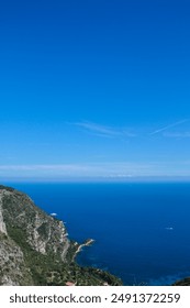 Panoramic coastal view with dramatic cliffs and deep blue ocean extending to the horizon under a cloudless sky. The rugged coastline and lush greenery create a striking contrast