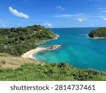 A panoramic coastal view from Windmill Viewpoint in Phuket overlooks Ya Nui Beach and the headlands near Promthep Cape, where a winding road follows the ridge above a turquoise bay