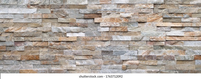 Panoramic detail of a stone wall made of bright, rough facing stones in different gray and brown color shades