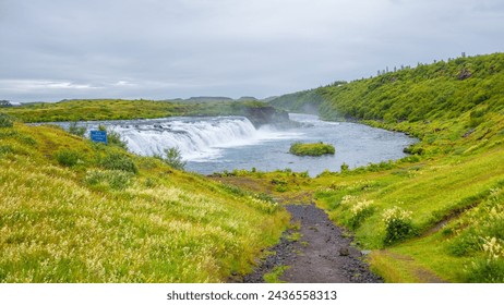 Panoramic with Faxafoss waterfall with dramatic sky and green hills. Beautiful Icelandic landscape, huge cliff, water cascade and rock in moss