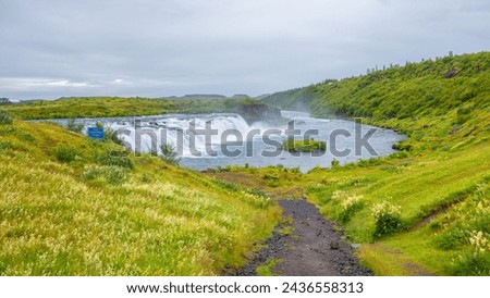 Panoramic with Faxafoss waterfall with dramatic sky and green hills. Beautiful Icelandic landscape, huge cliff, water cascade and rock in moss