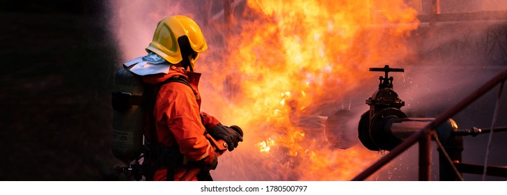 Panoramic Firefighter use water fog type fire extinguisher to fight with fire flame from oil pipeline leak and explosion on oil rig and natural gas station. Firefighter and industrial safety concept.