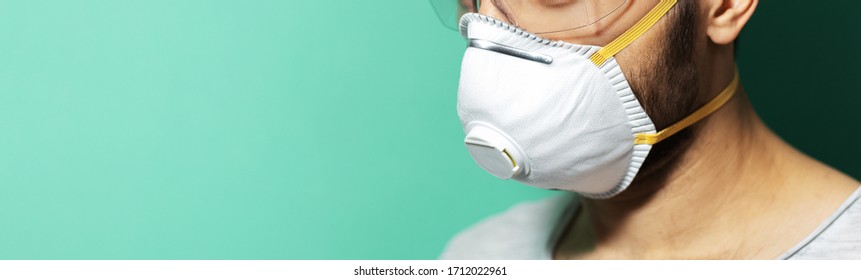 Panoramic Half Face Portrait Of Guy Wearing Respiratory Medical Mask And Safety Goggles Against Coronavirus On Aqua Menthe Color Background With Copy Space.