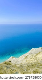 Panoramic high angle view of the vast blue ocean meeting the rugged cliffside under a bright clear summer sky