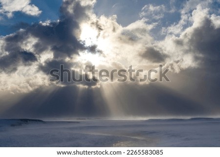 Panoramic high level view over snow covered landscape with river and mountains in Iceland with dramatic cloudscape of dark snowclouds making way for strong sunrays with blue sky 