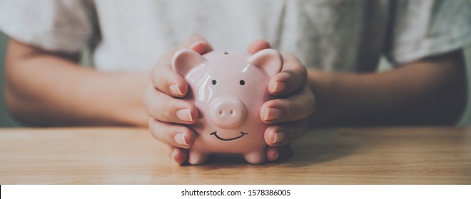 Panoramic image, Man hand holding piggy bank on wood table. Save money and financial investment - Powered by Shutterstock