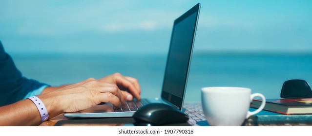 Panoramic Image Man Hands Typing Text On Laptop Computer In Front Blue Sea And Clear Sky. Concept Remote Work, Freelance. Design Banner With Copy Space