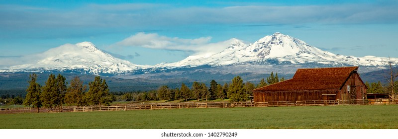 A panoramic image of the snow covered three sisters mountains with a barn and pasture in foreground, near Bend, Oregon