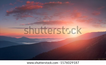 Panoramic landscape of colorful sunrise in the mountains. View on foggy hills covered by forest. Concept of the awakening wildlife.