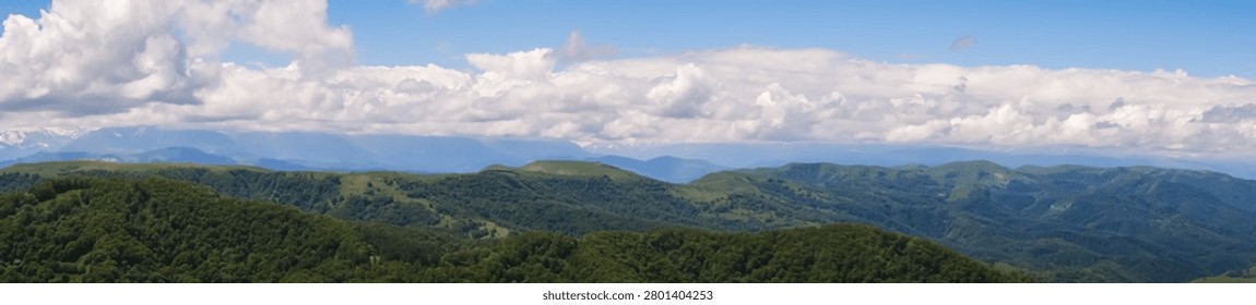 Panoramic landscape featuring rolling green mountains beneath a clear blue sky filled with white clouds, showcasing a tranquil outdoor scene