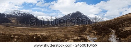 A panoramic landscape image looking across the wide Glen Dee in the Scottish Highlands. The Devil's Point stands darkly to the right, with Momadh Mor and Beinn Bhrotain to its left all covered in snow