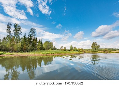 Panoramic landscape on a sunny day on the river with the sky in the clouds and the reflection in the water. - Shutterstock ID 1907988862