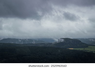 A panoramic landscape photo features a dramatic, overcast sky over rolling hills and a distant mountain range, with dark, ominous clouds creating a sense of tension and a grim, atmospheric mood. - Powered by Shutterstock