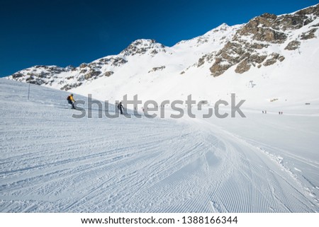 Panoramic landscape valley view with skiers going down a ski slope piste in winter alpine mountain resort