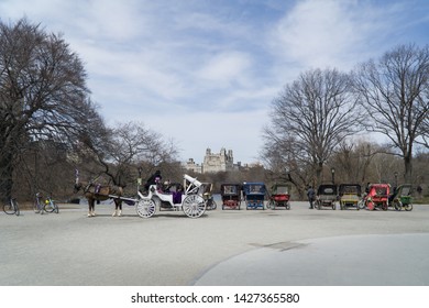 Panoramic Landscape View Over Central Park Lake, A Romantic White Carriage With A Fancy Brown Horse Is Passing Next To Other Carriages Waiting For Tourists, Manhattan, New York City Street, Usa.