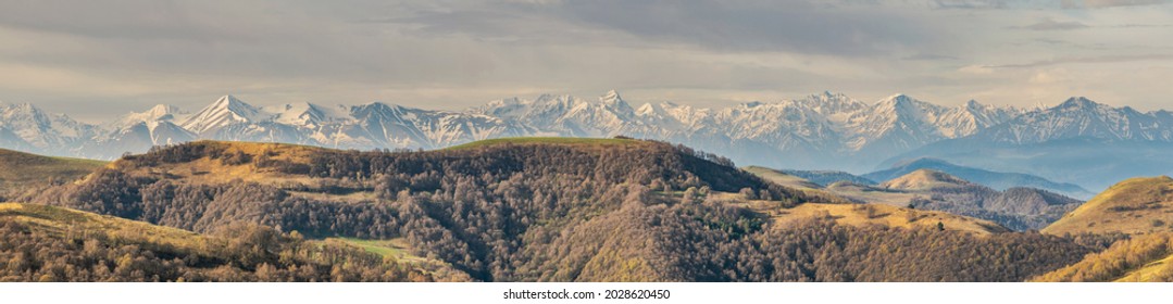 Panoramic landscape view over Gum-bashi mountain pass, with new green and old brown grass on cliffs, dark clouds before the storm, Сaucasus mountian range and Elbrus mountain. Karachay-Cherkessia - Shutterstock ID 2028620450