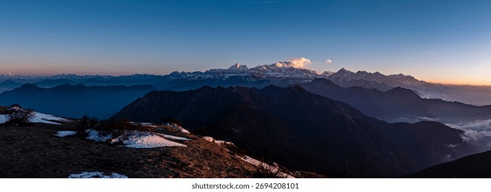 A panoramic of a mesmerizing skyline of a mountain range with snow-covered peaks against the blue sky