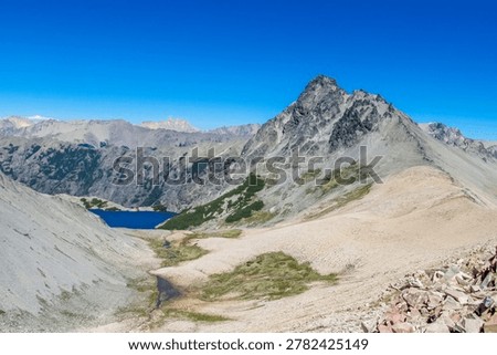 Panoramic mountain landscape of Cerro Catedral in the Patagonian Andes near San Carlos de Bariloche. Known for its jagged granite peaks resembling cathedral spires, this iconic mountain destination is surrounded by alpine lakes, rugged ridges, and dense forests characteristic of northern Patagonia. Snow-covered slopes in winter transform the area into one of South America’s premier ski resorts, while summer reveals hiking trails, rocky terrain, and sweeping panoramic views. The dramatic combination of mountain scenery, changing weather, and pristine wilderness creates a striking natural environment ideal for outdoor adventure. Perfect for themes of travel, mountaineering, skiing, and landscape photography, the image captures the beauty and grandeur of the Argentine Andes.