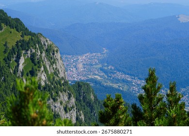 Panoramic mountain view with rocky cliffs and dense forests, overlooking a small town nestled in the valley below.