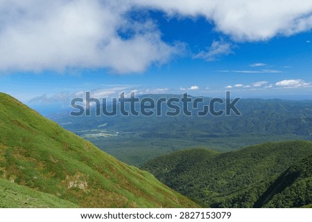 Panoramic mountain view while hiking Mount Shari in eastern Hokkaido, Japan. A panoramic view of green mountains and vast forests seen while hiking Mount Shari in eastern Hokkaido, Japan. This expansive landscape represents mountain trekking, outdoor adventure, nature, and scenic tourism in northern Japan.