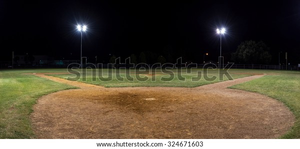 Panoramic night photo of an empty baseball field\
at night with the lights on taken behind home plate and looking out\
over the pitcher\'s\
mound.