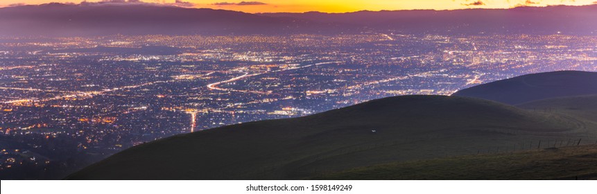 Panoramic night view of San Jose, Silicon Valley; the downtown area buildings visible on the right; green hills partially blocking the view; San Francisco Bay Area, California
