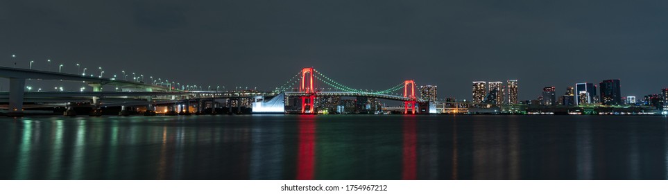 Panoramic nightview of Rainbow Bridge illuminated in red as a sign of Tokyo Alert, coronavirus alert for Tokyo area, in Odaiba Japan.