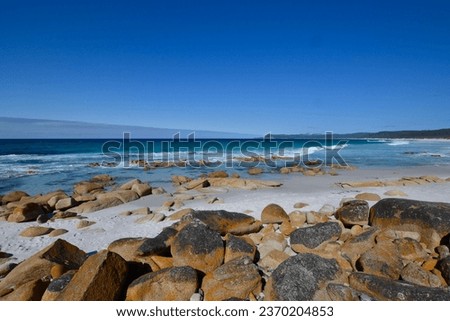 Panoramic ocean view of Friendly Beaches on Freycinet Peninsula in Tasmania with iconic orange lichen rocky shore in the foreground and surf waves in the distance