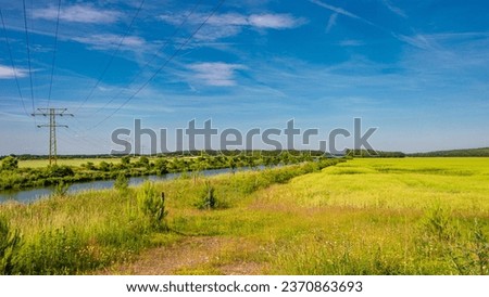 Panoramic over beautiful grass field farm landscape with a huge electricity grid power line pylon and a Elbe Canal at sunny day and blue sky with sunset colors in Germany.