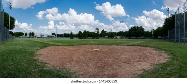 A Panoramic Photo Of A Baseball Field Looking From Behind Home Plate Out Across Pitcher's Mound And The Diamond To Outfield Wiht Fluffy Clouds In The Blue Sky Overhead.