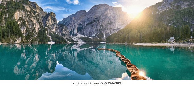 Panoramic photo of Lago di Braies, Pragser Wildsee in the Dolomites. View of the whole green-blue lake through wooden boats on the mountain peak and the setting sun. 