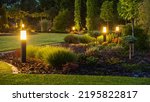 Panoramic Photo of LED Light Posts Illuminated Backyard Garden During Night Hours. Modern Backyard Outdoor Lighting Systems.