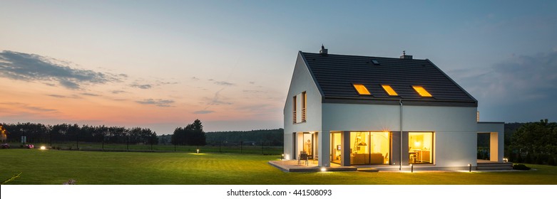 Panoramic photo of modern house with outdoor and indoor lighting, at night