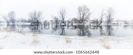 panoramic photo of a winter river with snowy banks and ice.