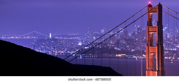 A panoramic photograph of The Golden Gate Bridge and San Francisco, CA at night. 