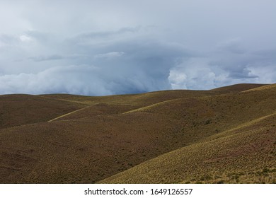 Panoramic Photograph Of A Landscape Divided In Two. Below The Greenish Mountains With Little Vegetation And Above A Cloudy Sky With A Possible Storm. North Argentina.