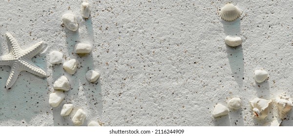 Panoramic sand background with seashells, starfish, cord and pebbles. Off white banner, panorama with stones on textured sand surface. Summertime monochromatic flat lay. Summer beach decorations. - Powered by Shutterstock