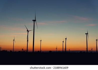 Panoramic scenic landscape view new modern wind turbine farm power generation station against fiery warm sunset sky field. Clean sustainable zero emission alternative electricity windfarm industry