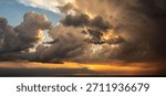 Panoramic seascape view of dramatic stormy sky with dark cumulonimbus clouds and bright orange sunlight beams over the calm water horizon during a beautiful sunset evening on the sea coast.